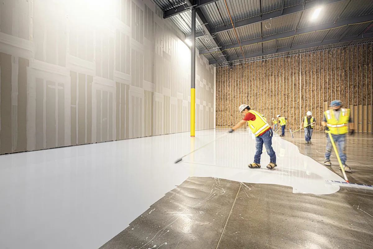 Crew squeegeeing a fresh epoxy coat across a warehouse floor