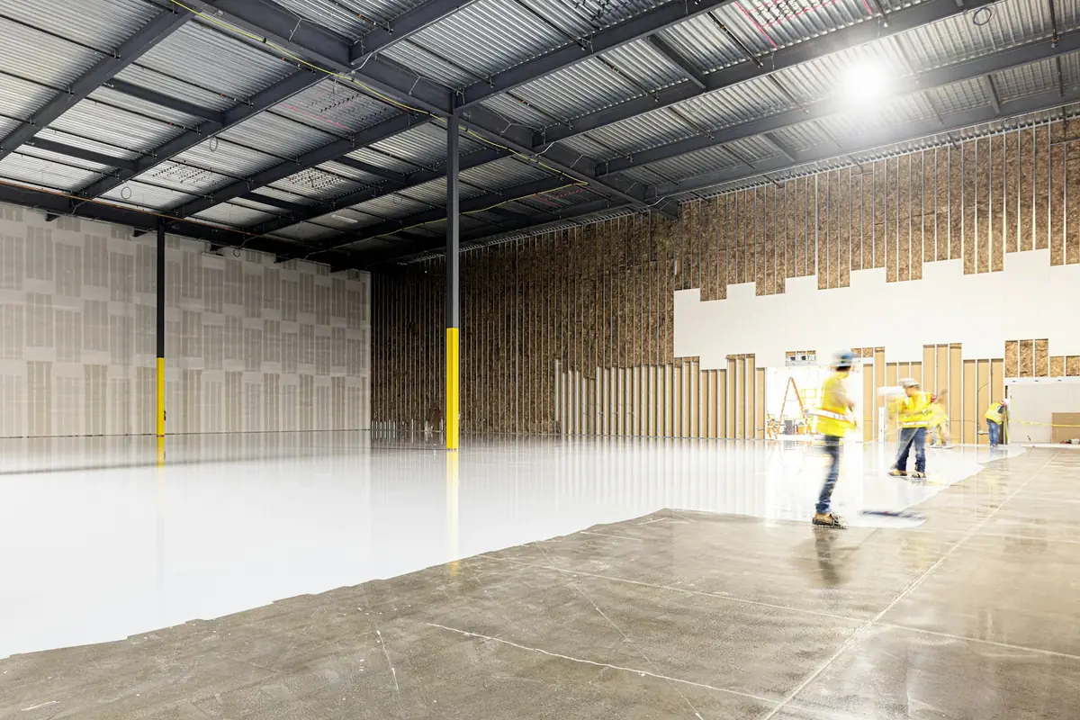 Crew applying a white epoxy coating across a large warehouse floor